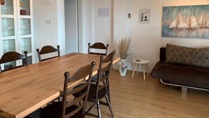 A dining area with a wooden table and chairs, a small side table with a vase, a sofa, and a painting on the wall.