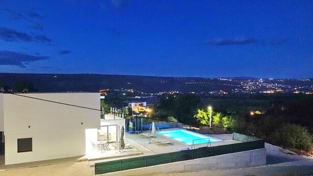 Une maison moderne dotée d’une piscine, d’un balcon et offrant une vue sur la ville la nuit.