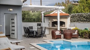 A poolside area with lounge chairs, a dining set, and a barbecue.
