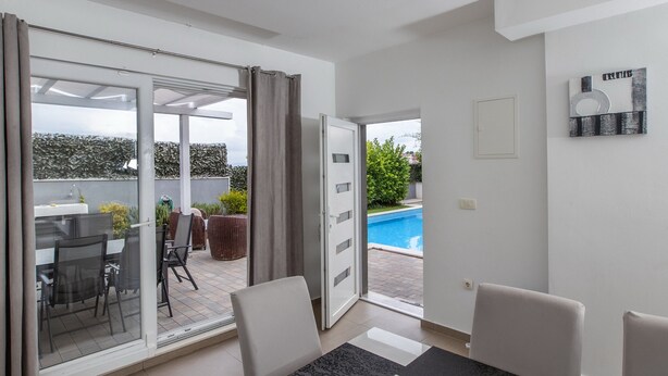 A modern living room with a glass door leading to a balcony with outdoor furniture and a pool.