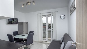 A modern living room with a sofa, a dining table with chairs, a flat-screen TV, and a refrigerator.
