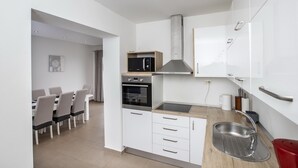 A modern kitchen with white cabinets, a built-in oven, a microwave, and a stainless steel sink.