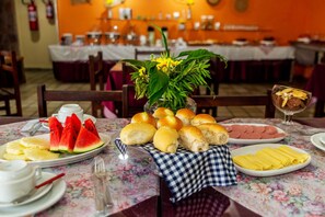 Una mesa de comedor con diversos alimentos, como rebanadas de sandía, bollos de pan y un plato de jamón.