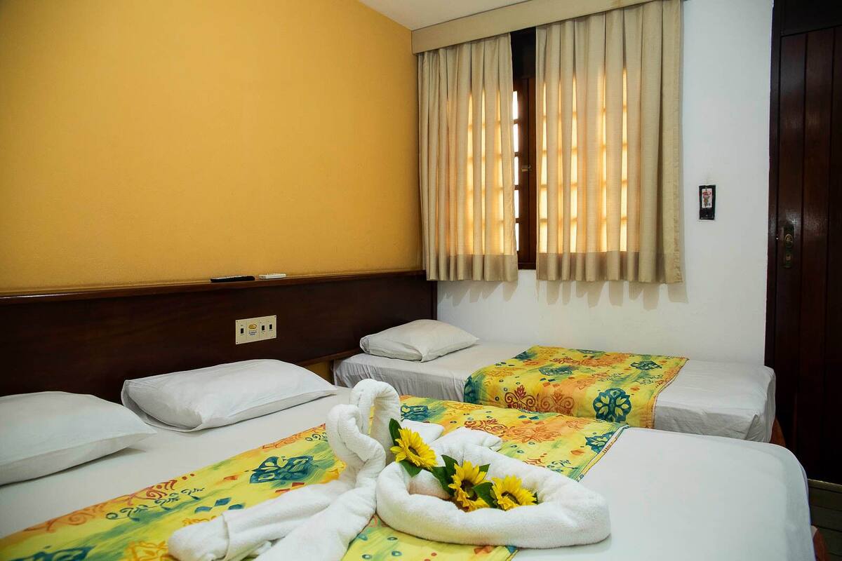 A hotel room with two single beds, each with a floral bedspread and white pillows. There are towels and sunflowers on the beds.
