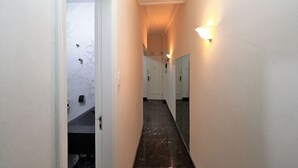 Ein schmaler Gang mit einer Marmorwand, einem schwarzen Fliesenboden und einer Leuchte auf der rechten Seite.