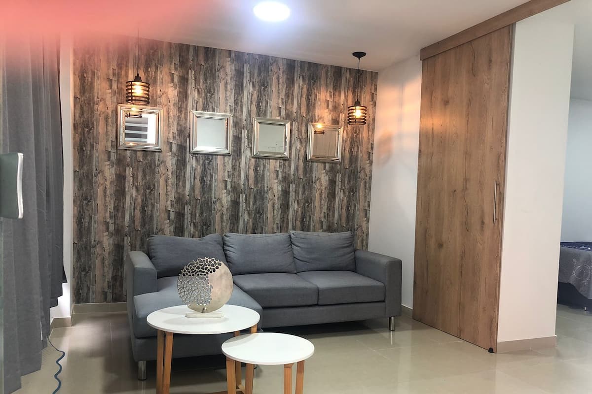 A modern living room with a grey sofa, two white round tables, and a wooden wall with framed mirrors.