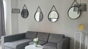 Ein modernes Wohnzimmer mit einem grauen Modulsofa, einem runden Couchtisch und drei Wandspiegeln.