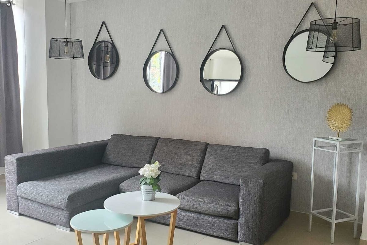 A modern living room with a grey sectional sofa, a round coffee table, and three wall-mounted mirrors.
