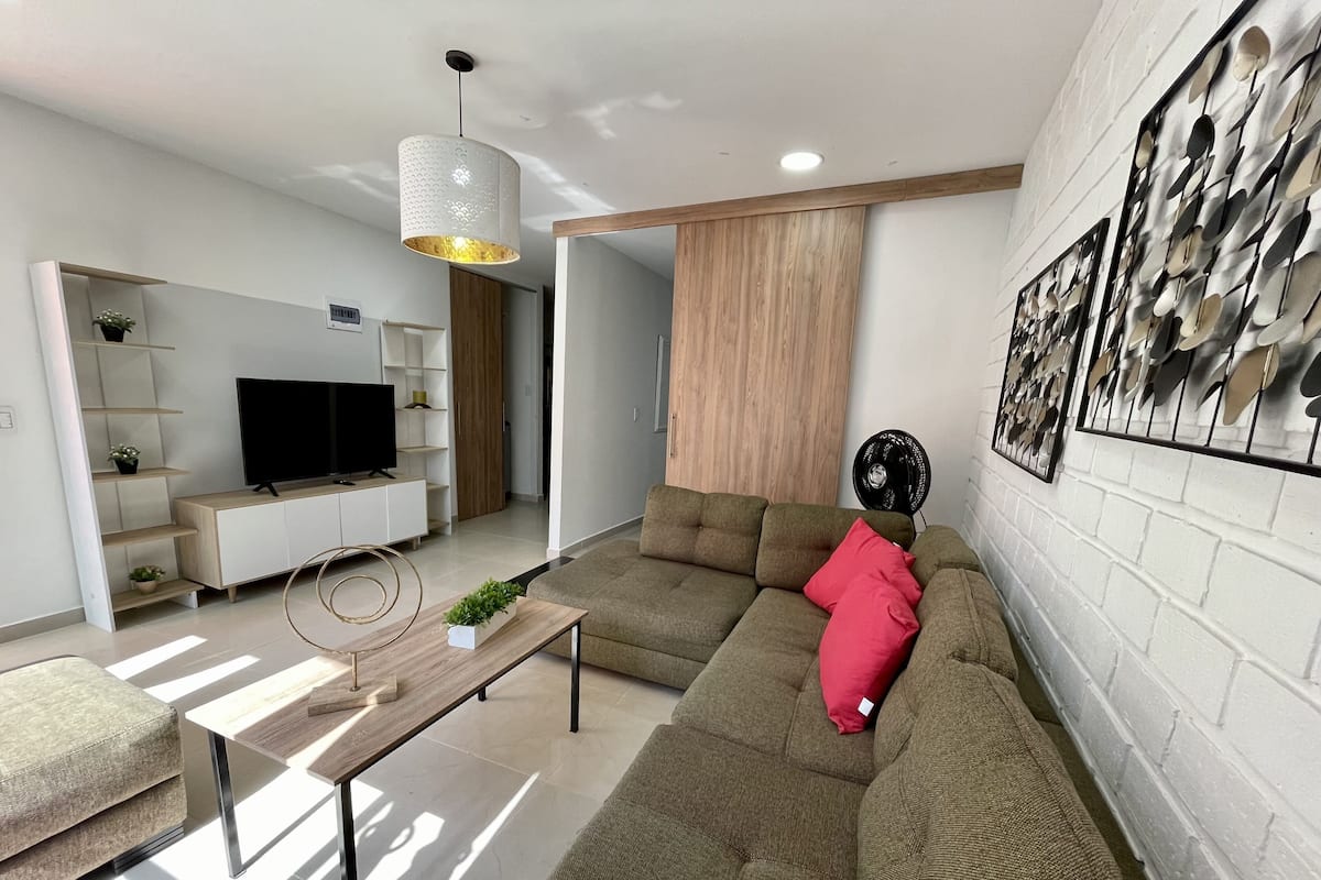 A modern living room with a sectional sofa, a flat-screen TV, a coffee table, and a decorative wall piece.