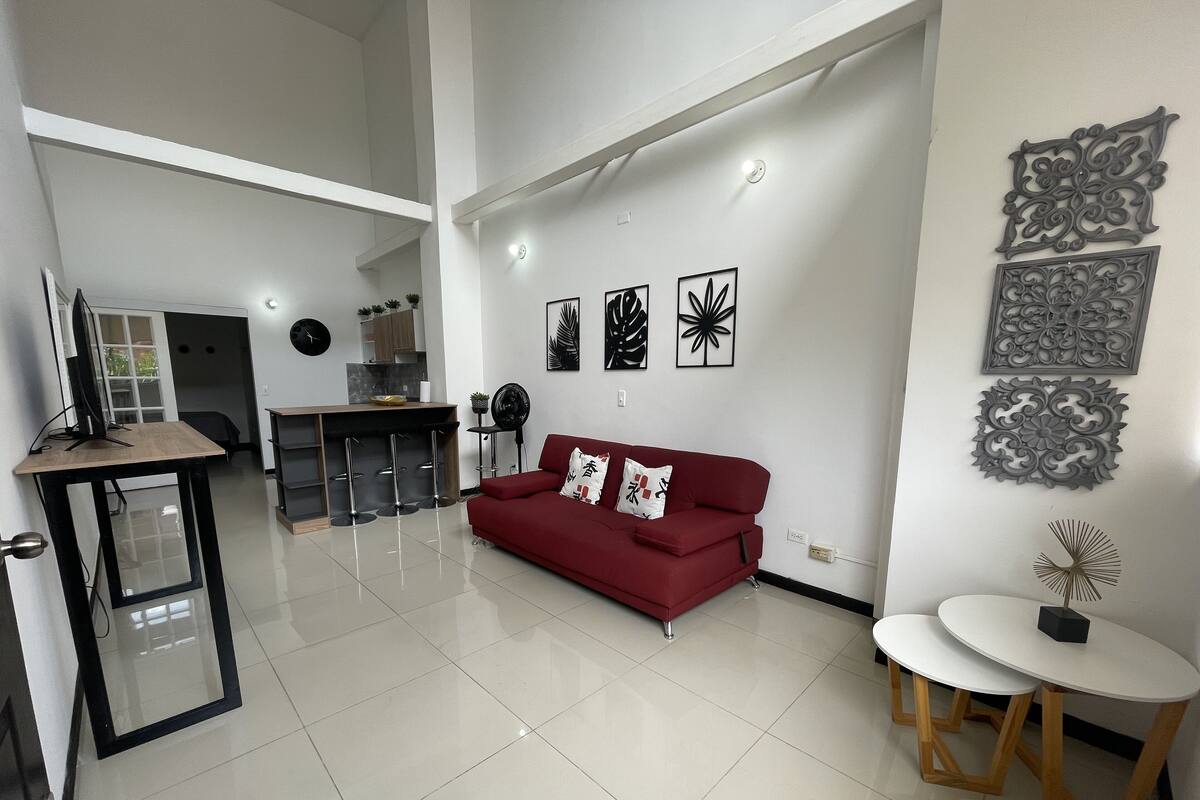 A modern living room with a red sofa, a small round table, and a kitchen in the background.
