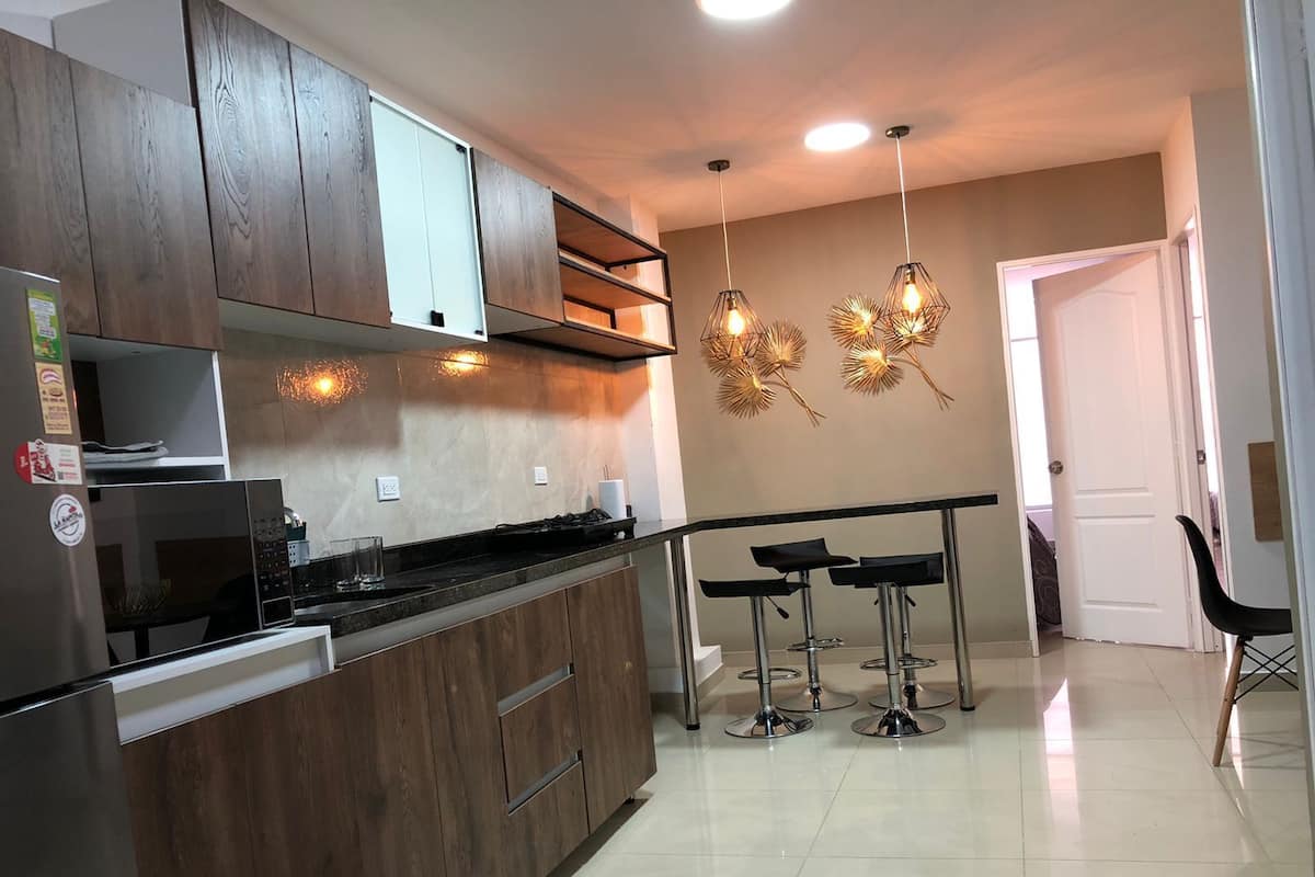 A modern kitchen with wooden cabinets, a built-in microwave, and a gas stove. There are three bar stools and a hanging light fixture.