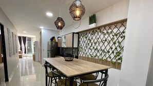 Eine moderne Küche mit einem Holzespeisetisch, vier Stühlen, Pendelleuchten, einem Kühlschrank und einer dekorativen Pflanzenwand.