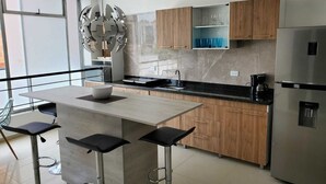 Eine moderne Küche mit einer zentralen Kochinsel, Barhocker, Holzschränken und einem Edelstahlkühlschrank.