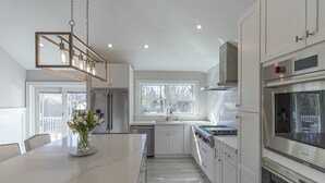 A modern kitchen with a marble island, stainless steel appliances, and a large window providing natural light. - Chic Hamptons Home near beach! (Hampton Bays)