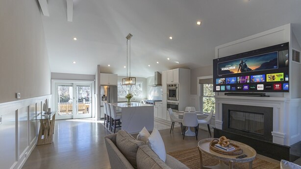 A modern living room with a large flat-screen TV, a fireplace, and a dining area with a glass table. - Chic Hamptons Home near beach! (Hampton Bays)