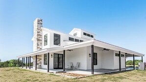 A modern two-story house with a covered patio, large windows, and a stone chimney. - Lone Star River Ranch- Large Luxury Venue for Conferences & Retreats - sleeps 44 (Brady)