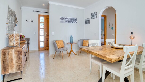 A dining area with a wooden table and white chairs, a small round table with a blue vase, and a cabinet with jars. - LA BELLESA: Beautiful house with private pool in l'Escala (L'Escala)