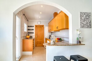 A compact kitchen with wooden cabinets, a built-in oven, and a small island with a sink. - LA BELLESA: Beautiful house with private pool in l'Escala (L'Escala)