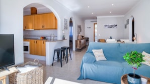 A modern living space with a kitchen, a blue sofa, a television, and a potted plant. - LA BELLESA: Beautiful house with private pool in l'Escala (L'Escala)