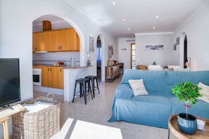 A modern living space with a kitchen, a blue sofa, a television, and a potted plant. - LA BELLESA: Beautiful house with private pool in l'Escala (L'Escala)