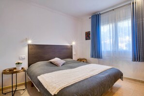 A bedroom with a large bed, a bedside table with a lamp, a small table with a plant, and a window with curtains. - LA BELLESA: Beautiful house with private pool in l'Escala (L'Escala)