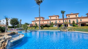 Ein Pool mit gewölbter Kante, umgeben von einer gepflegten Rasenfläche und Palmen.
