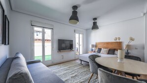 A modern hotel room with a sofa, dining table, and a TV mounted on the wall. - Ático del Oso · Terraza privada en Lavapiés (Madrid)
