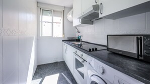 A kitchen with white cabinets, a microwave, a stove, and a window. - Ático del Oso · Terraza privada en Lavapiés (Madrid)