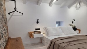 A modern bedroom with a bed, bedside tables, a hanging light, and a stone wall. - Stone build Suite with private small pool (Skiathos)