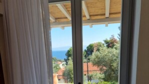A room with a sliding glass door leading to a balcony with a view of the sea and buildings. - Stone build Suite with private small pool (Skiathos)