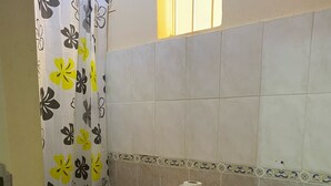 A bathroom with a toilet, a black trash bin, a sink, and a shower curtain with a floral pattern.