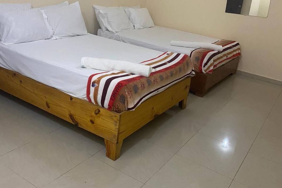 A room with two single beds, a wooden headboard, a tiled floor, and a mirror on the wall.