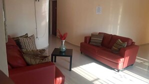 A living room with two red sofas, a small table with a vase, and a door in the background.