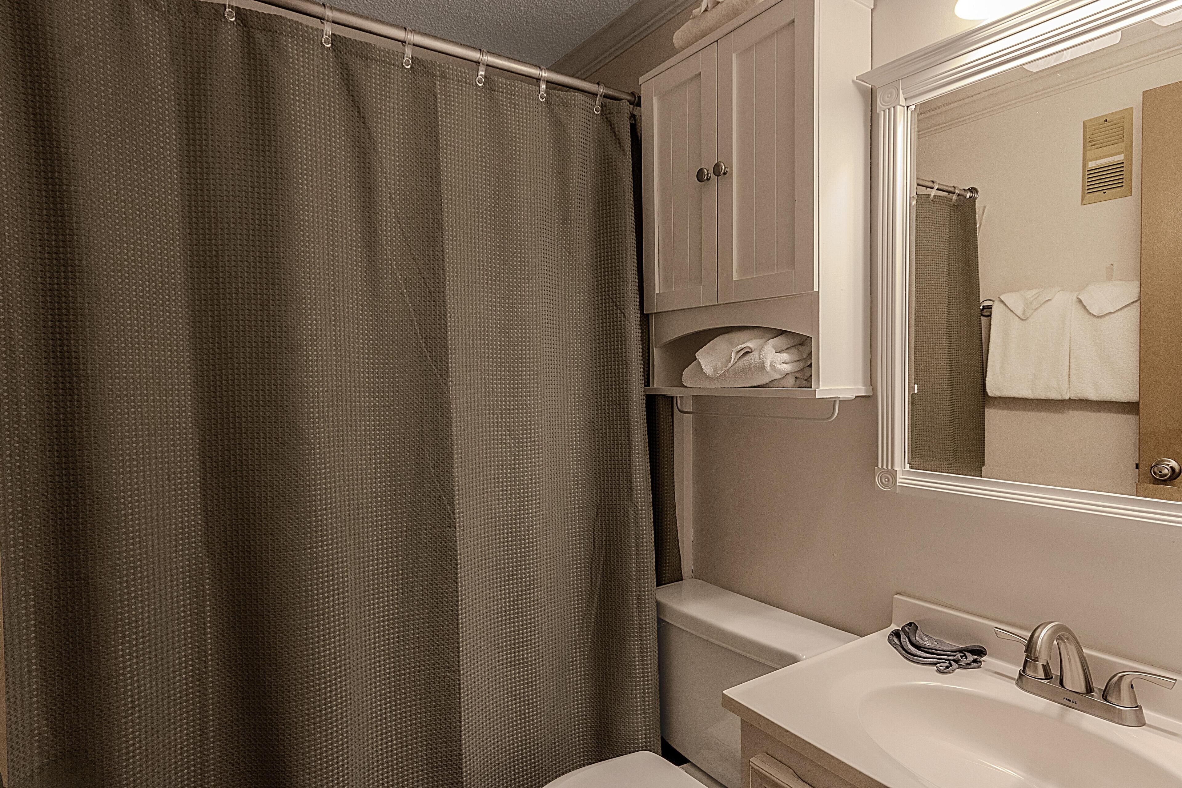Une salle de bain avec un rideau de douche, un lavabo avec un robinet et un miroir.