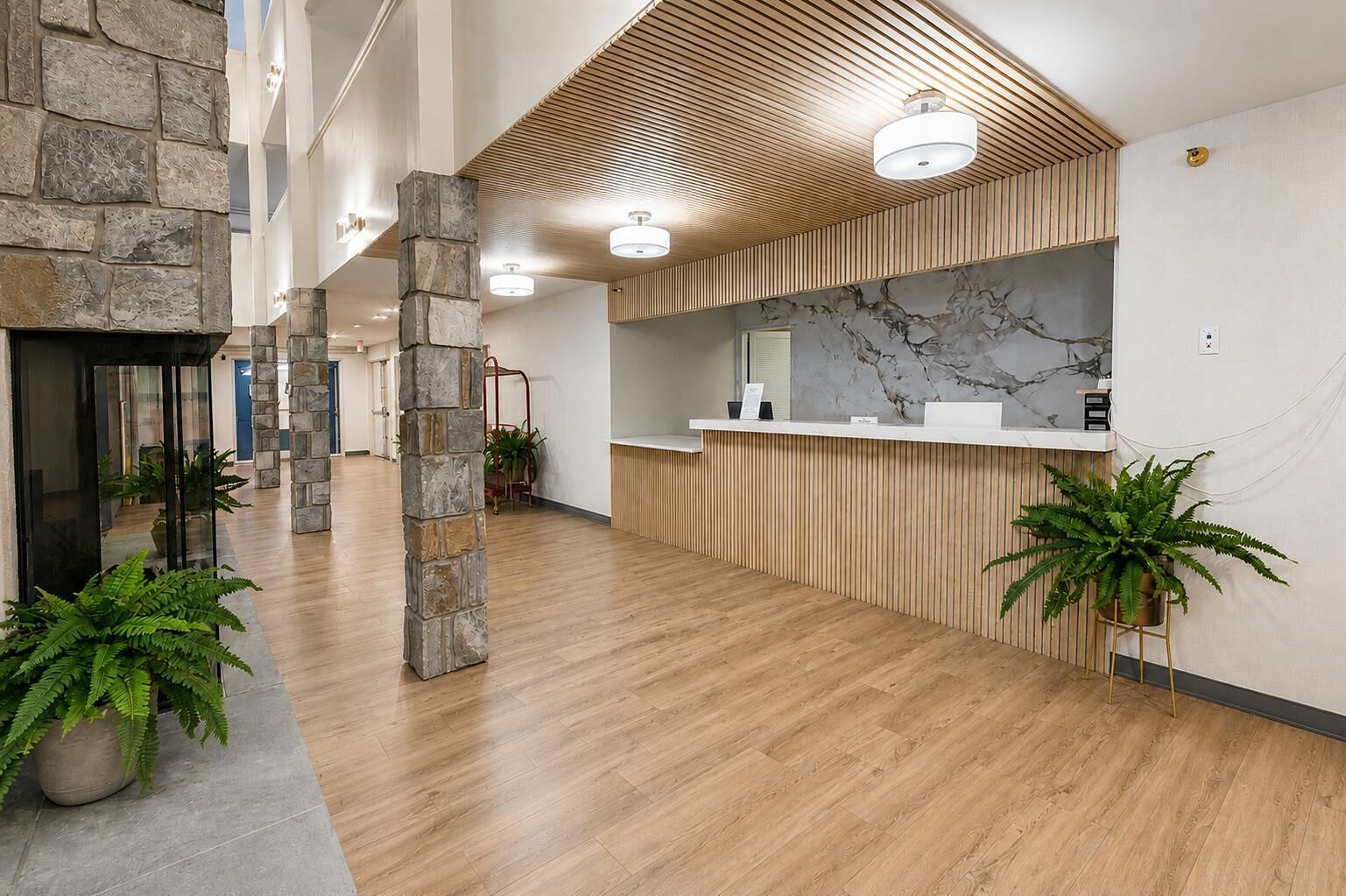 A spacious lobby with a reception desk, stone pillars, and potted plants.