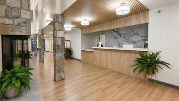 A spacious lobby with a reception desk, stone pillars, and potted plants.