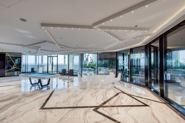 A spacious indoor area with a pool table, seating, and large windows offering views of the city.