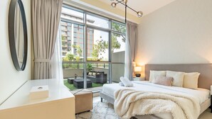 Habitación de hotel moderna con un ventanal grande, una cama con un edredón blanco mullido, una mesita de noche y una lámpara.