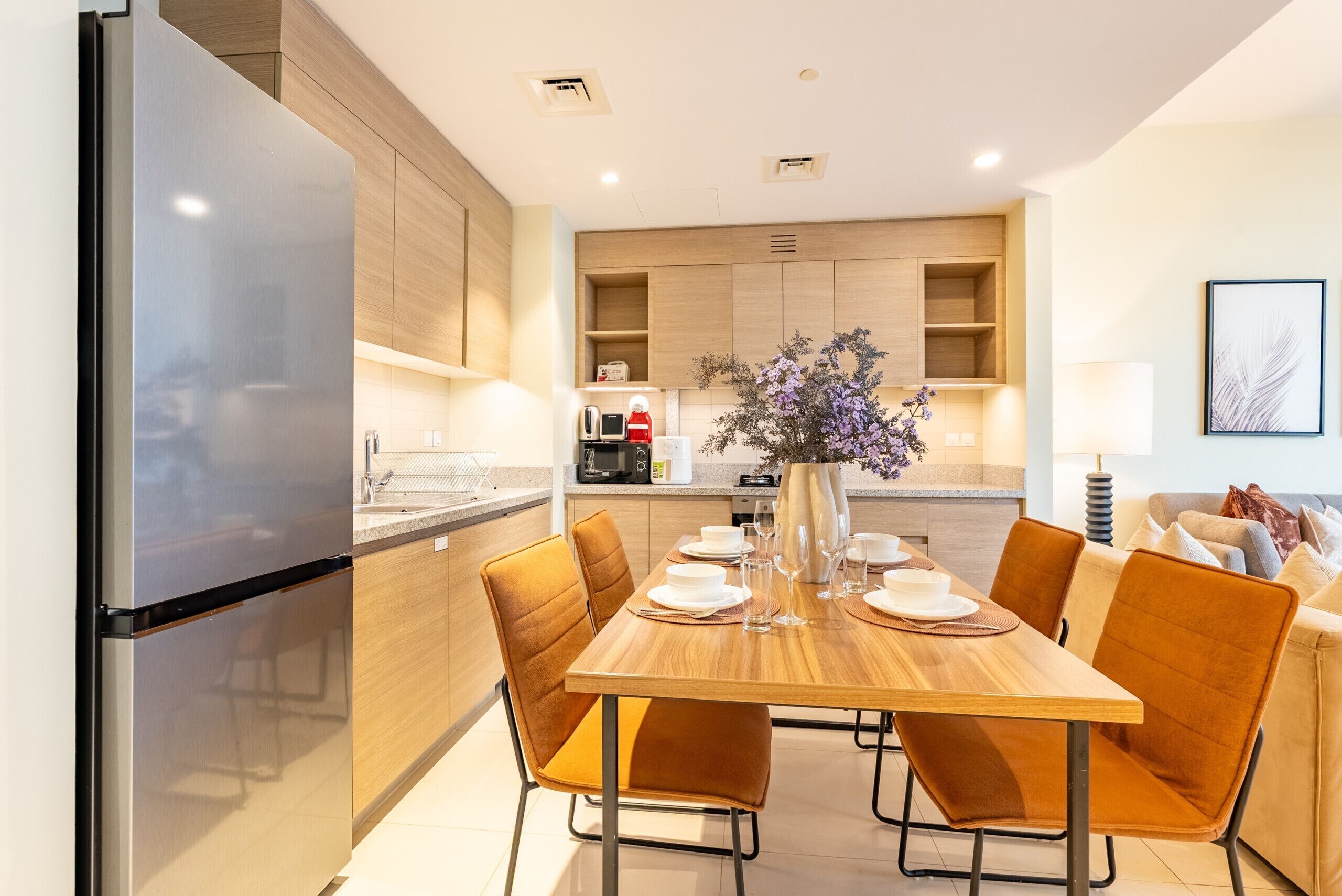 A modern kitchen with a built-in refrigerator, wooden cabinets, and a dining area with a table set for four.