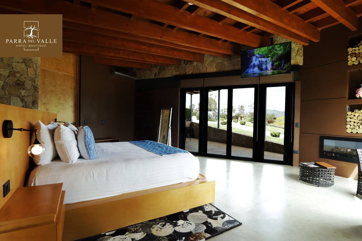 A bedroom with a large bed, a stone wall, a wooden ceiling, and a TV mounted on the wall.