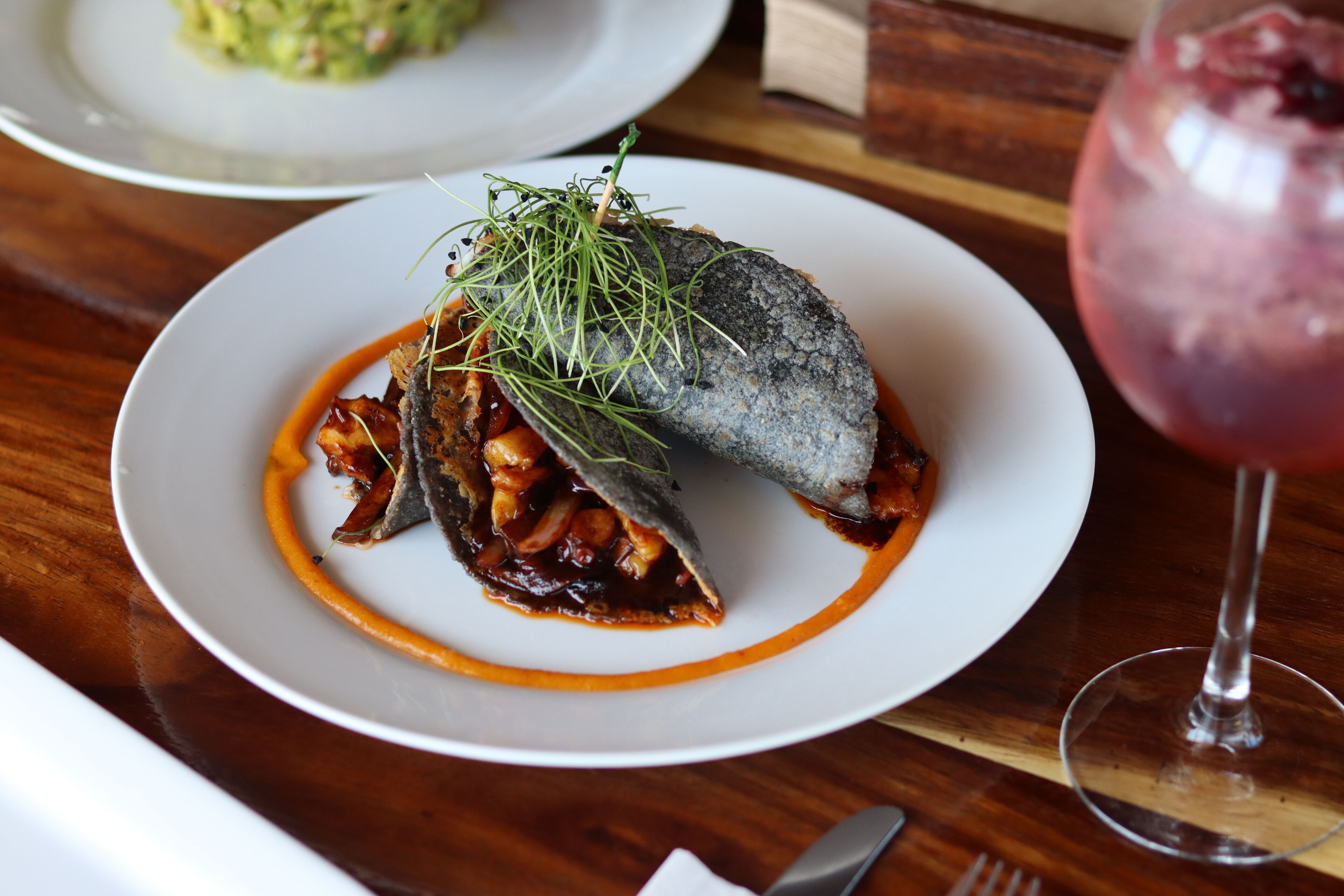 A plate of food with a fish, sauce, and garnish on a wooden table.