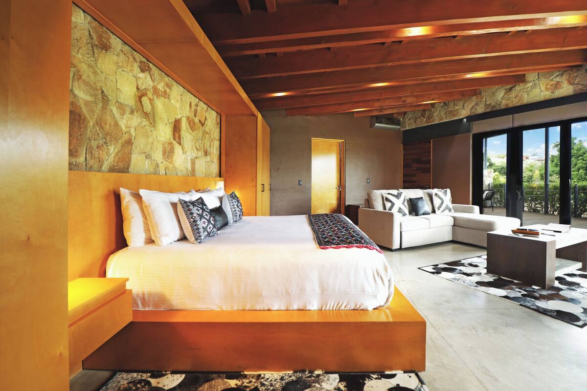 A modern bedroom with a large bed, a sofa, and a view of the outdoors.