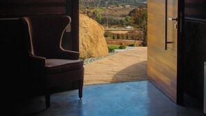 Puerta abierta que da a vistas de montañas, una silla en el interior y un sendero de piedra en el exterior.