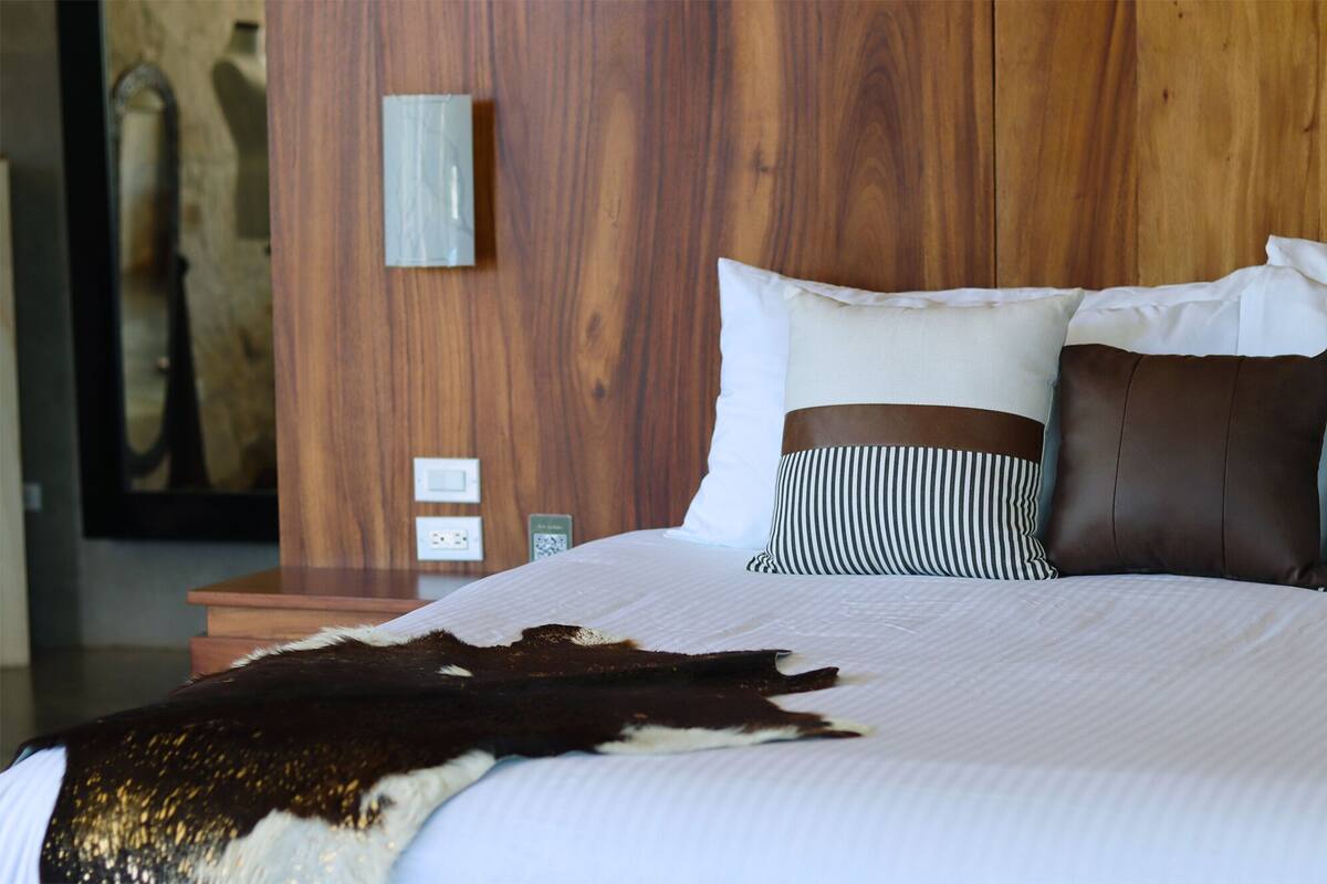 A hotel room with a wooden headboard, a white bedspread, and a cowhide blanket.