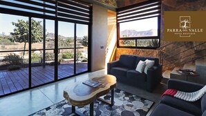 Un salón moderno con un amplio ventanal, una mesa de centro de madera, un sofá y una escalera que da a un área exterior.