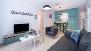 Ein modernes Wohnzimmer mit Flachbildfernseher, einer Couch, einem Couchtisch und einem Essbereich mit Tisch und Stühlen.