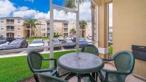 Ein Balkon mit rundem Tisch und Stühlen, der auf einen Parkplatz und Wohnhäuser blickt.