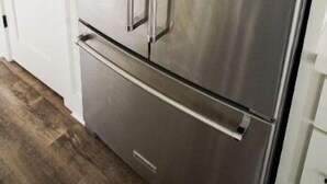 Un réfrigérateur en acier inoxydable dans une cuisine avec des armoires blanches et un plancher en bois.