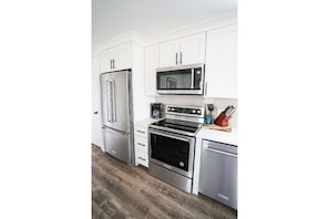 A modern kitchen with white cabinetry, stainless steel appliances, and a wooden floor.