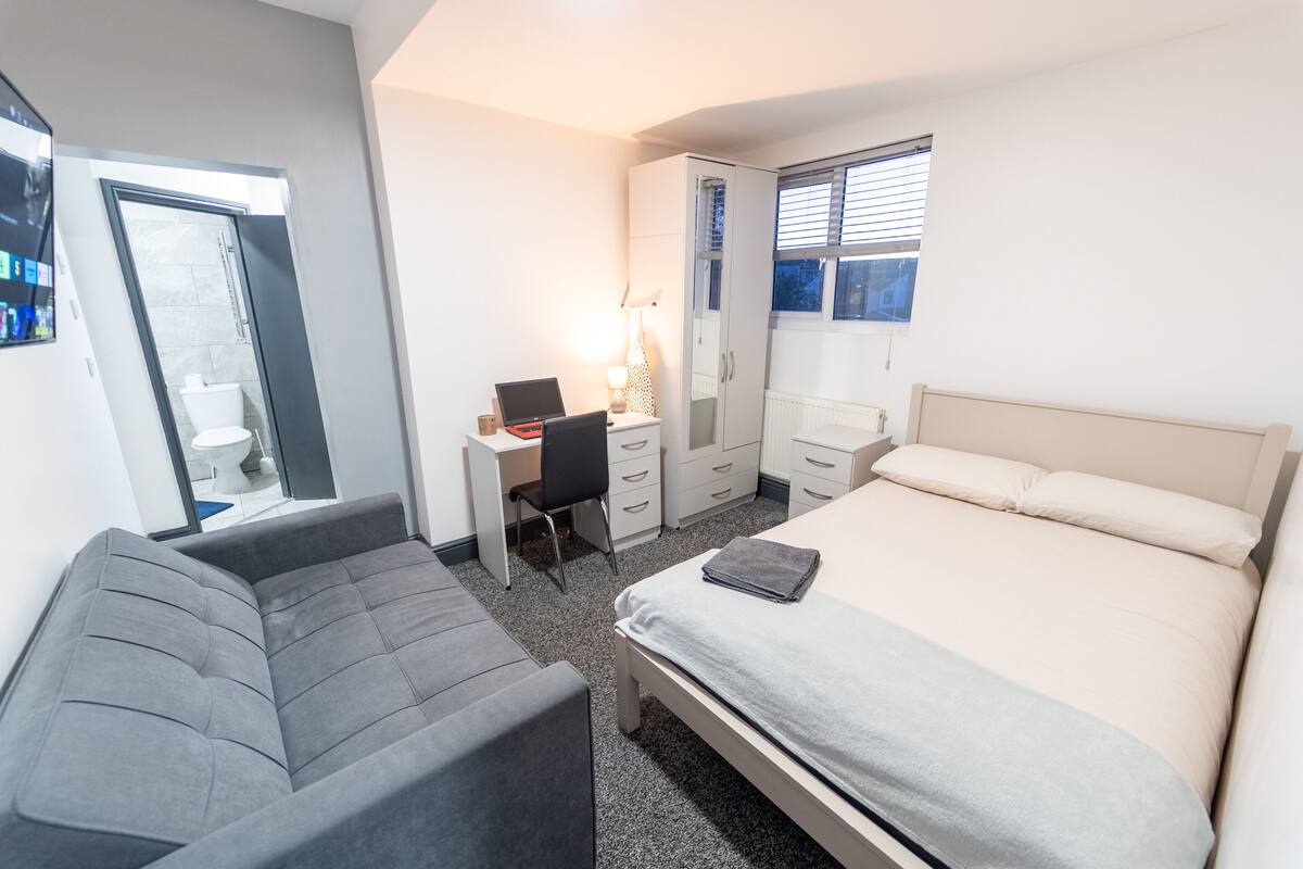 Ein modernes Schlafzimmer mit Bett, Sofa, Schreibtisch und Kleiderschrank.